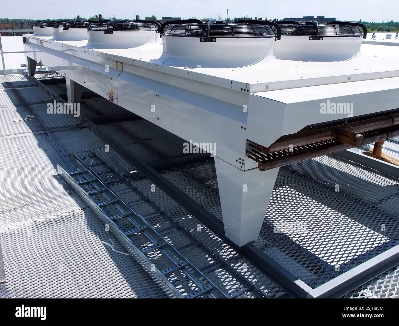 Un grand système de refroidissement industriel blanc avec ventilateurs se trouve au sommet d'une grille métallique sur un toit, sous un ciel dégagé, fournissant un contrôle climatique essentiel. Banque D'Images