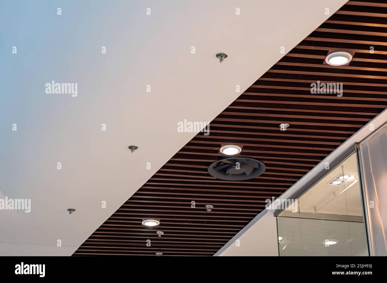 Un design de plafond moderne avec des panneaux blancs alternés et des lattes en bois sombre dispose d'un éclairage et d'une ventilation encastrés, créant une esthétique élégante. Banque D'Images