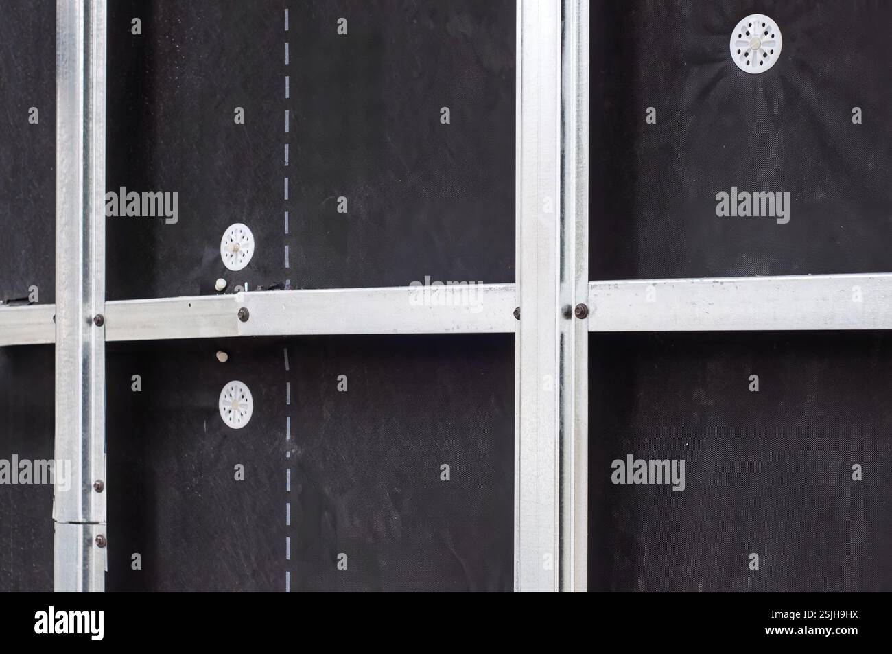 Gros plan d'un mur en cours de construction avec des poteaux métalliques et une membrane noire, prêt pour l'installation d'isolation. Banque D'Images