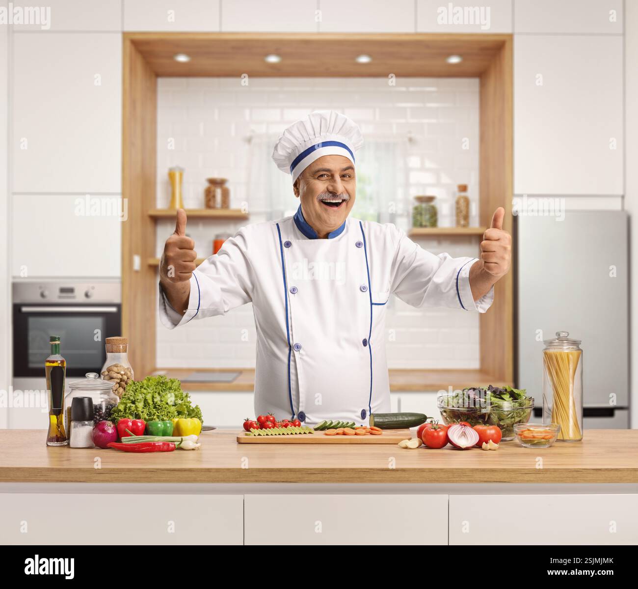 Joyeux chef masculin mature dans une cuisine montrant les deux pouces vers le haut Banque D'Images