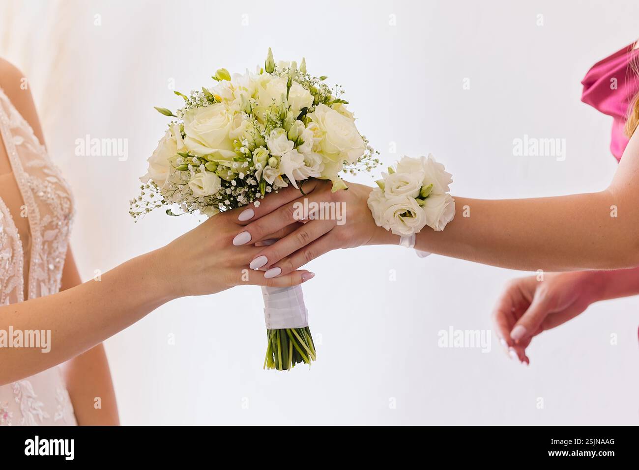 Gros plan d'une demoiselle d'honneur passant un bouquet floral blanc à la mariée. L'accent est mis sur leurs mains et les fleurs de mariage élégantes. Banque D'Images