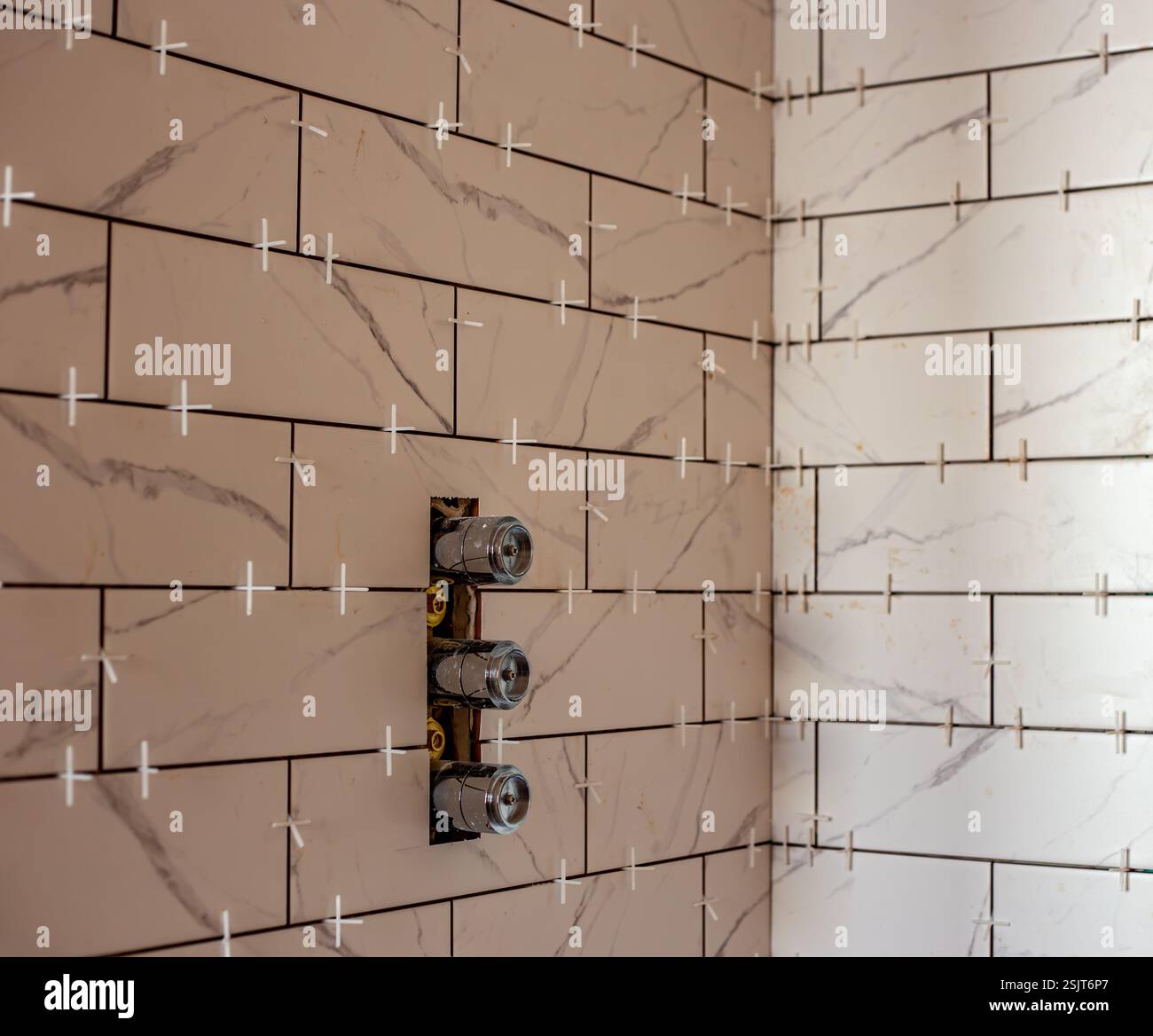 Mur de douche en construction avec des carreaux de marbre blanc et des entretoises en plastique dans le projet de rénovation de la maison Banque D'Images