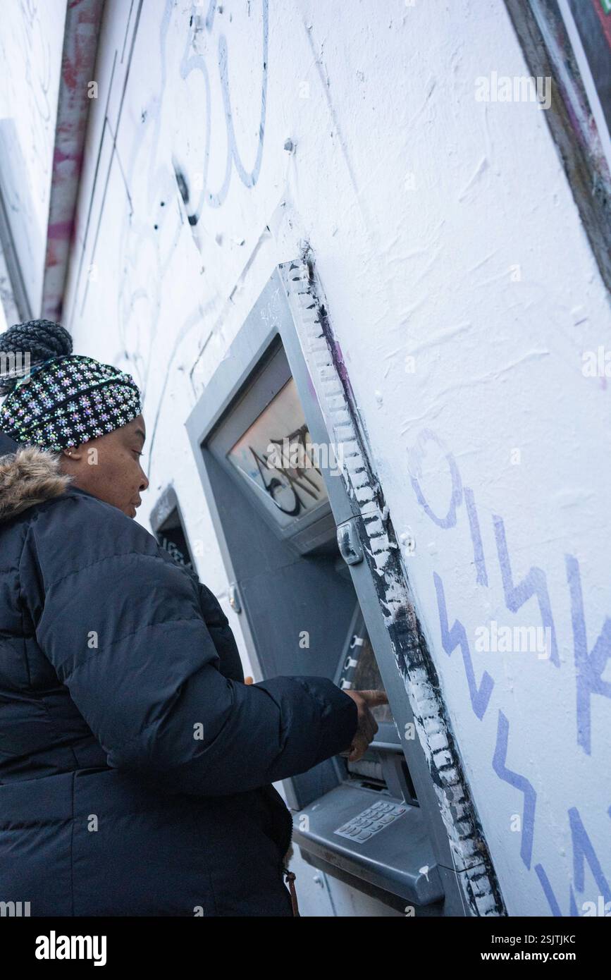 Une femme afro-caribéenne debout à un mur cashpoint dans le sud de Londres, Angleterre, Royaume-Uni. Banque D'Images