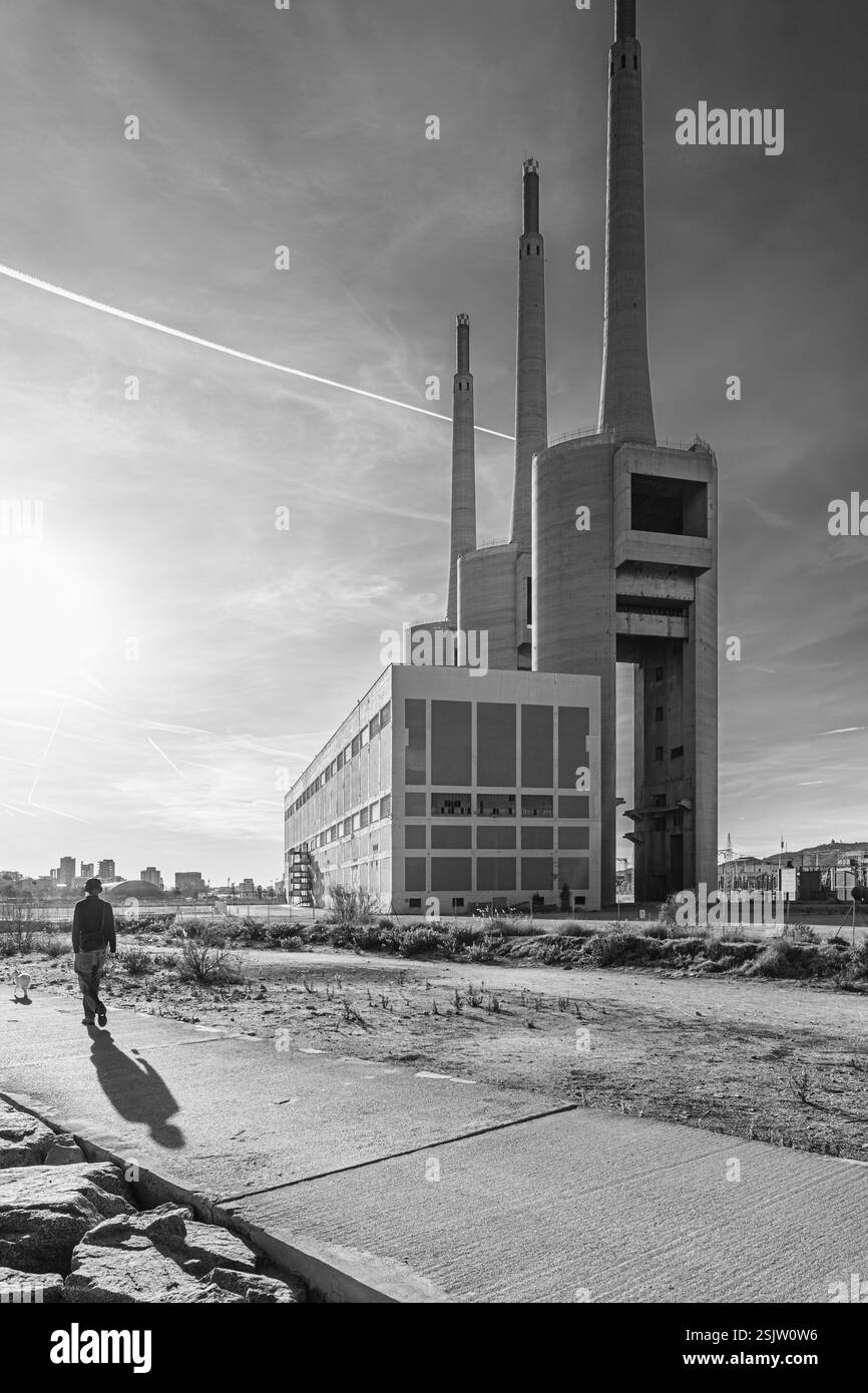 L’homme marche avec son chien sur un chemin en béton près de l’ancienne centrale thermoélectrique appelée Las Tres Chimeneas, à Sant Adrià de Besòs, en Espagne. Banque D'Images