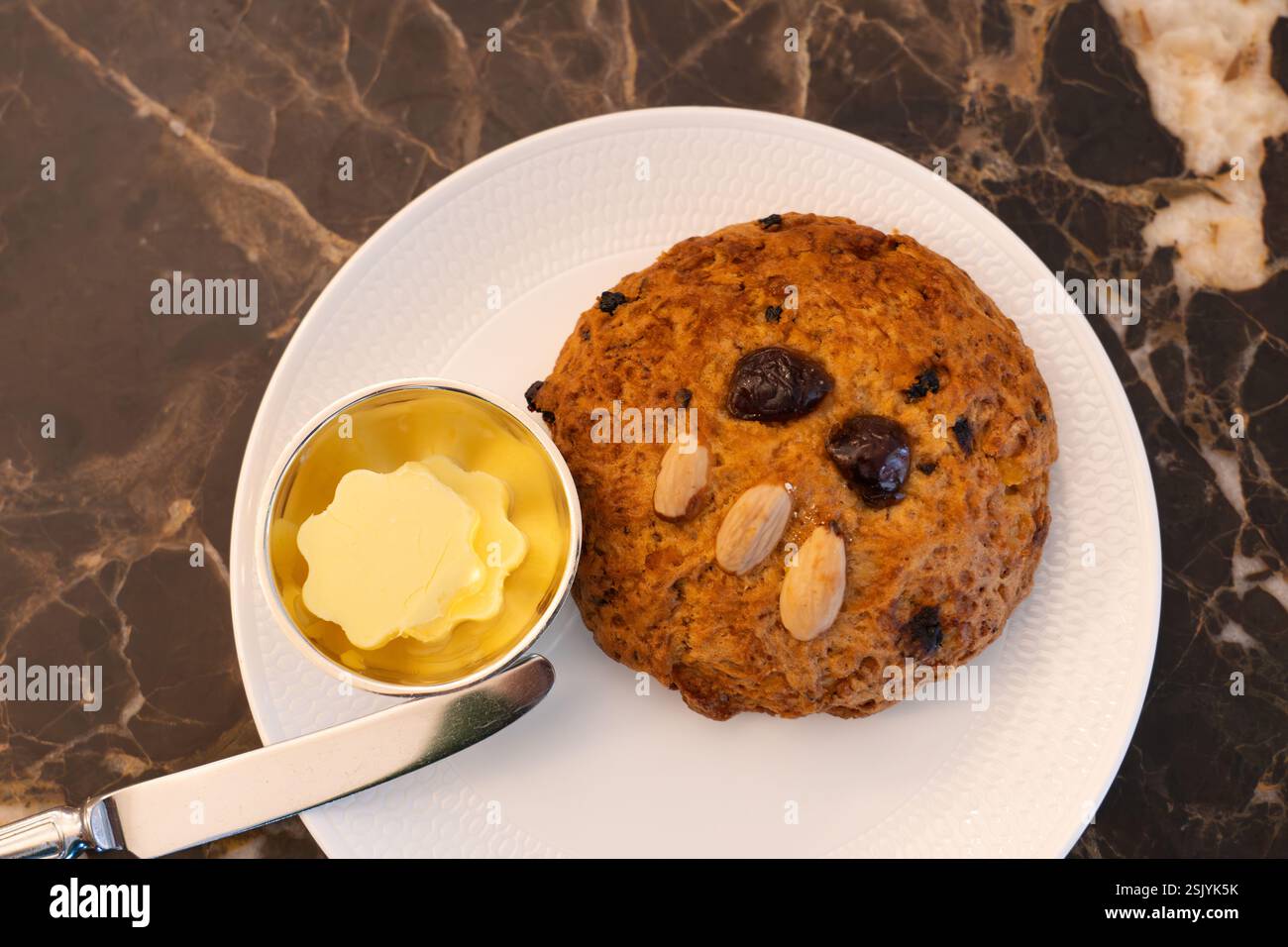 Célèbre scone rascal gras avec un visage décoré à la main à base de cerises et d'amandes avec un plat à beurre. Salons de thé Betty's Cafe à Harrogate, Angleterre Banque D'Images