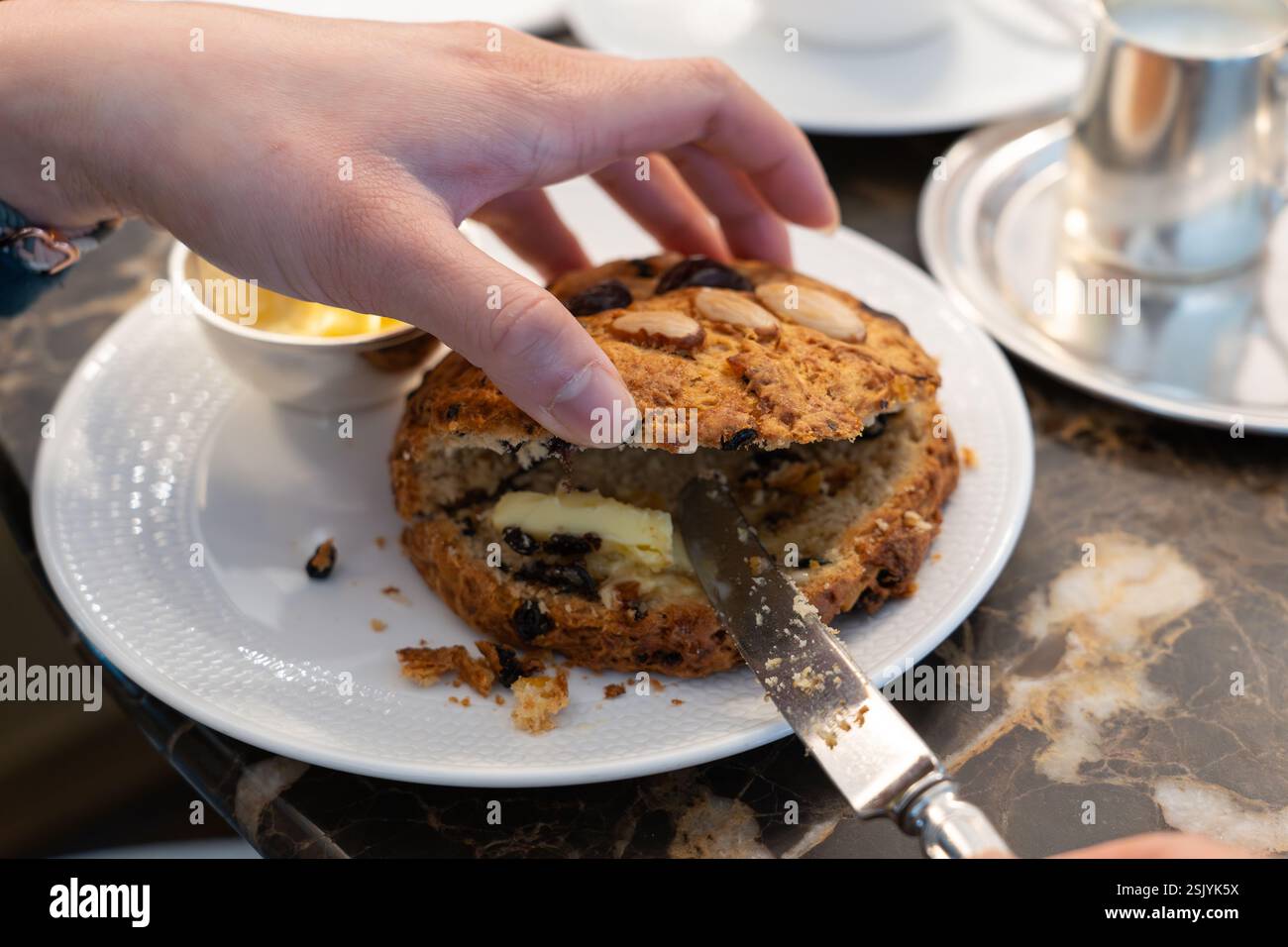Femme beurrant un célèbre scone rascal gras avec un visage fait à la main pour le thé de l'après-midi au Bettys Café Tea Rooms à Harrogate, en Angleterre Banque D'Images