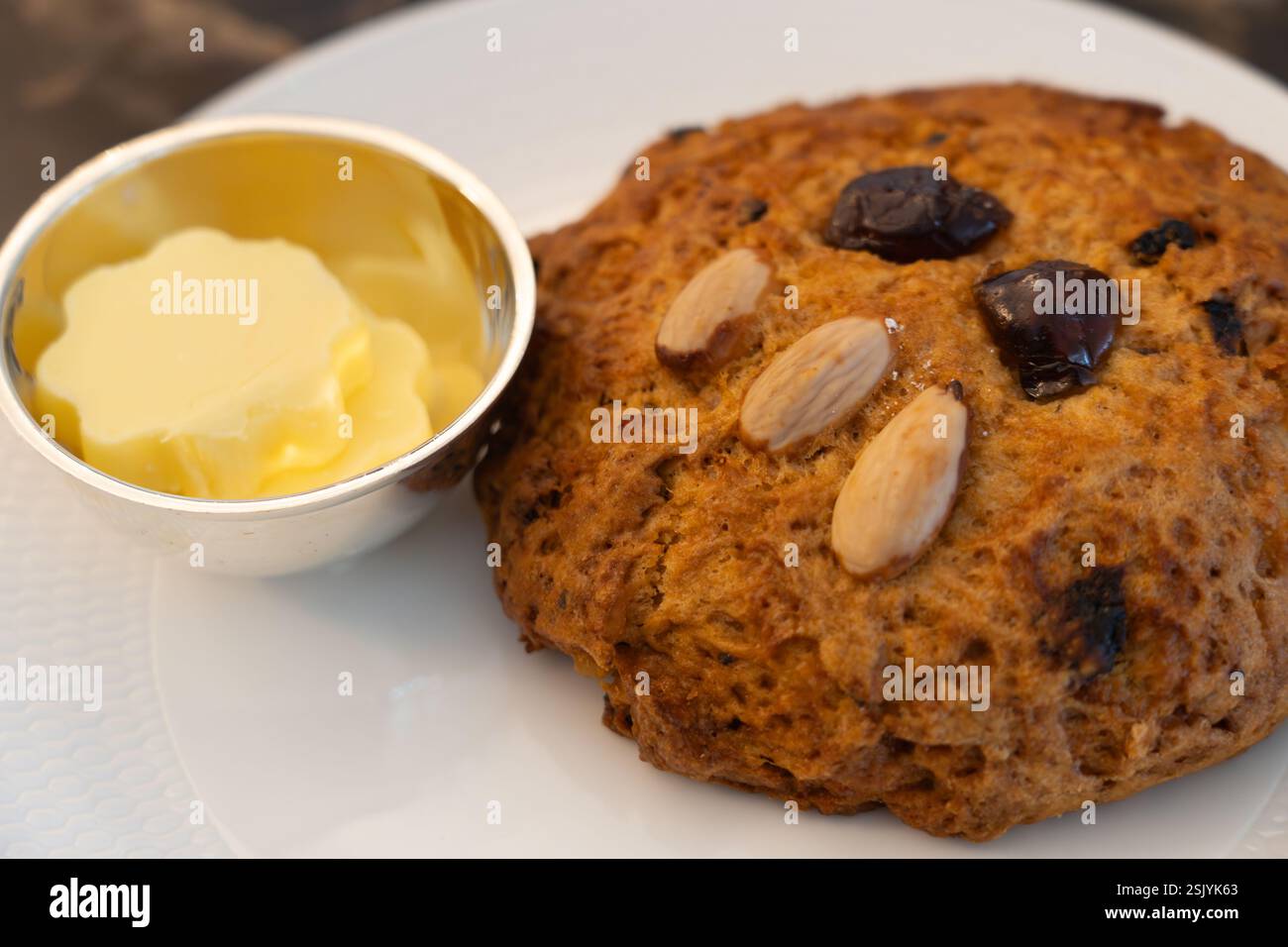Célèbre scone rascal gras avec un visage décoré à la main à base de cerises et d'amandes avec un plat à beurre. Salons de thé Betty's Cafe à Harrogate, Angleterre Banque D'Images