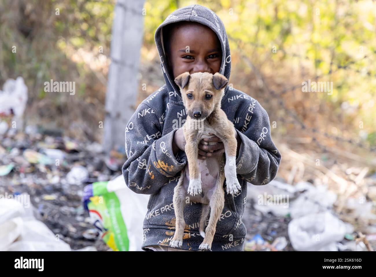 innocent pauvre gosse collecteur d'ordures avec sourire mignon et chien en main à l'extérieur le jour Banque D'Images