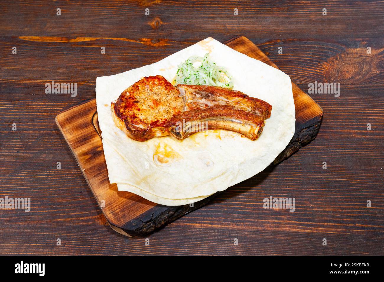 Un succulent porc grillé est présenté sur un plateau en bois parchemin bordé d'une salade fraîche. La présentation met en évidence les saveurs riches et te Banque D'Images