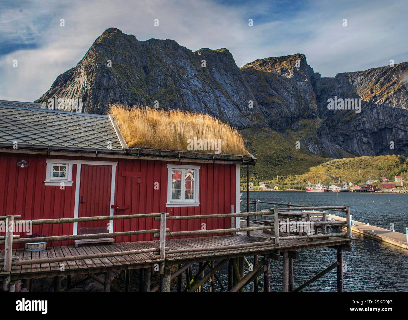 Cabine rouge sur ponton en bois au bord de la mer avec toit végétalisé dans le village norvégien Reine (reine) iwith fond de montagnes rocheuses dans l'archipel o Banque D'Images