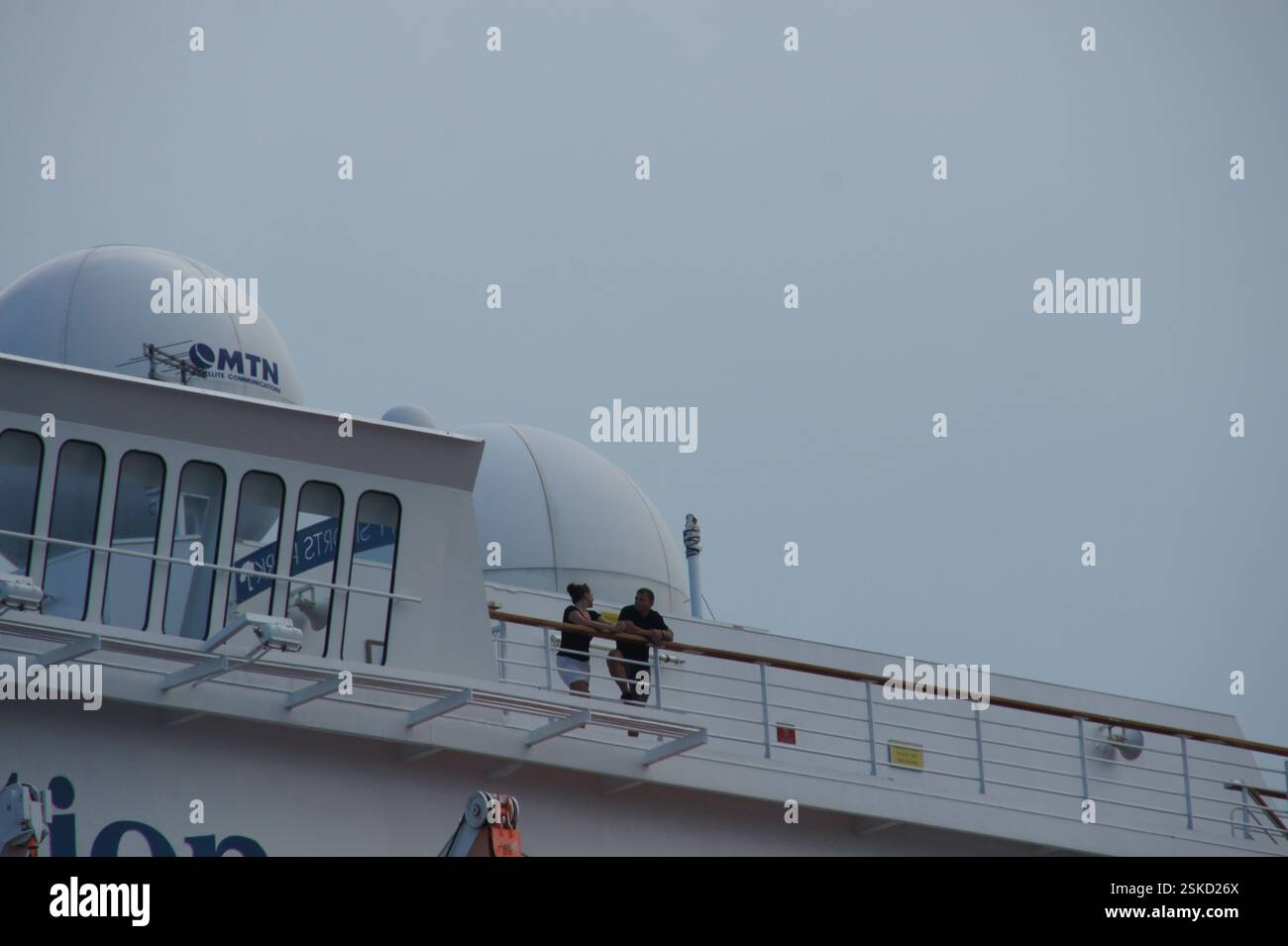 Pont de bateau de croisière avec deux personnes parlant. Logo MTN visible sur l'antenne parabolique. Personnes appréciant la vue ou discutant de l'itinéraire du navire. MTN pourrait aussi Banque D'Images