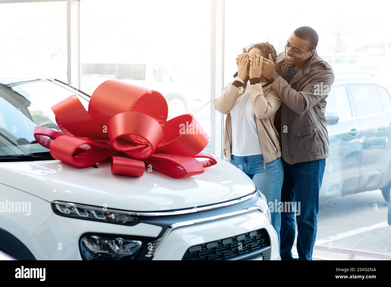 Propre voiture. Mari amrericain africain couvrant les yeux de sa femme montrant sa nouvelle auto dans le magasin de la concession. Espace vide Banque D'Images