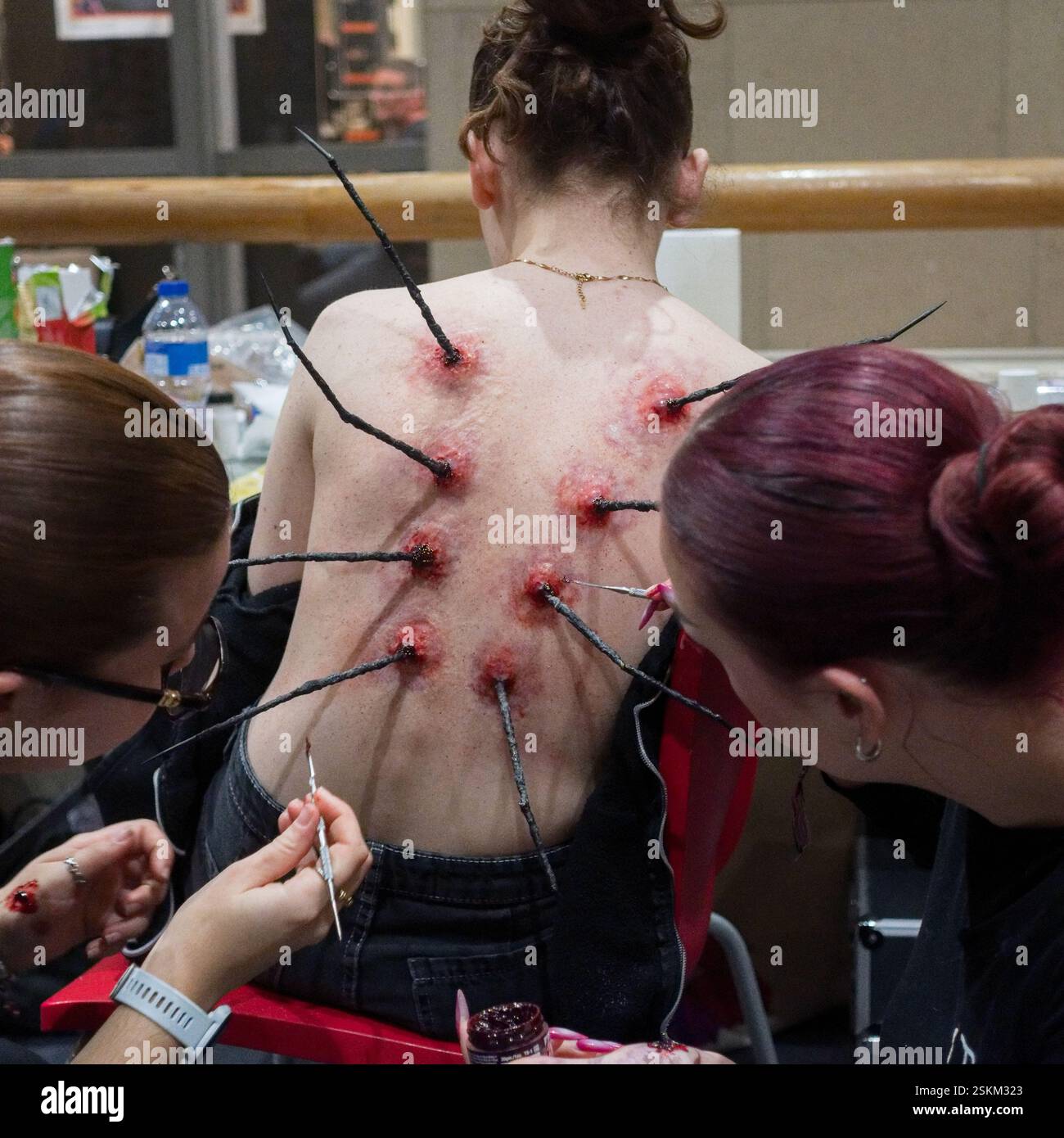 Effets spéciaux maquilleurs au travail créant des prothèses de plaies réalistes sur le dos d'acteur pour la production cinématographique ou théâtrale - Cinémathèque, Paris, 2025 Banque D'Images