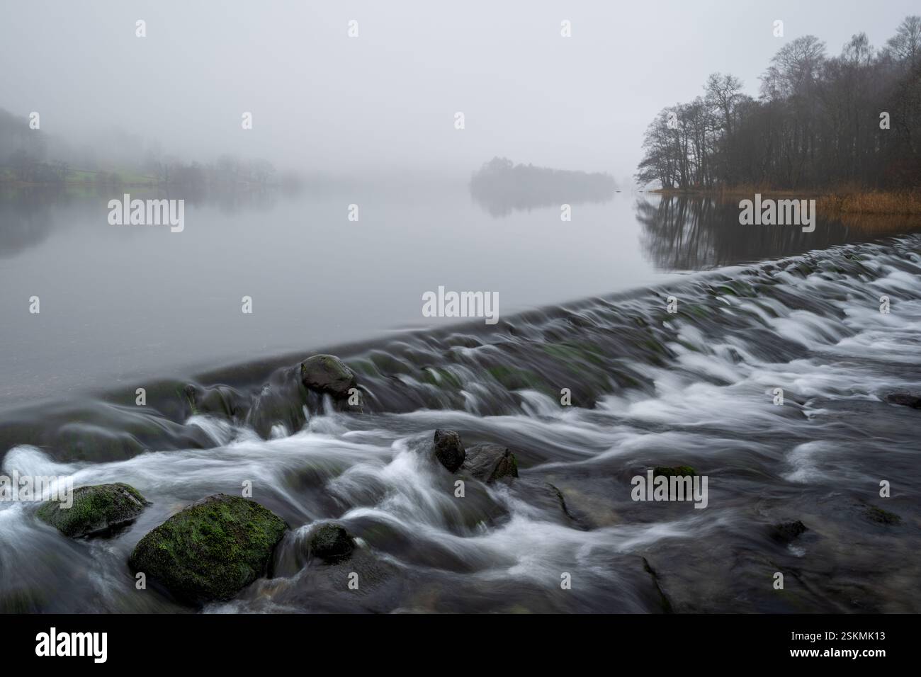 L'eau coule au barrage de Grasmere par un matin brumeux dans le Lake District, Royaume-Uni. Banque D'Images