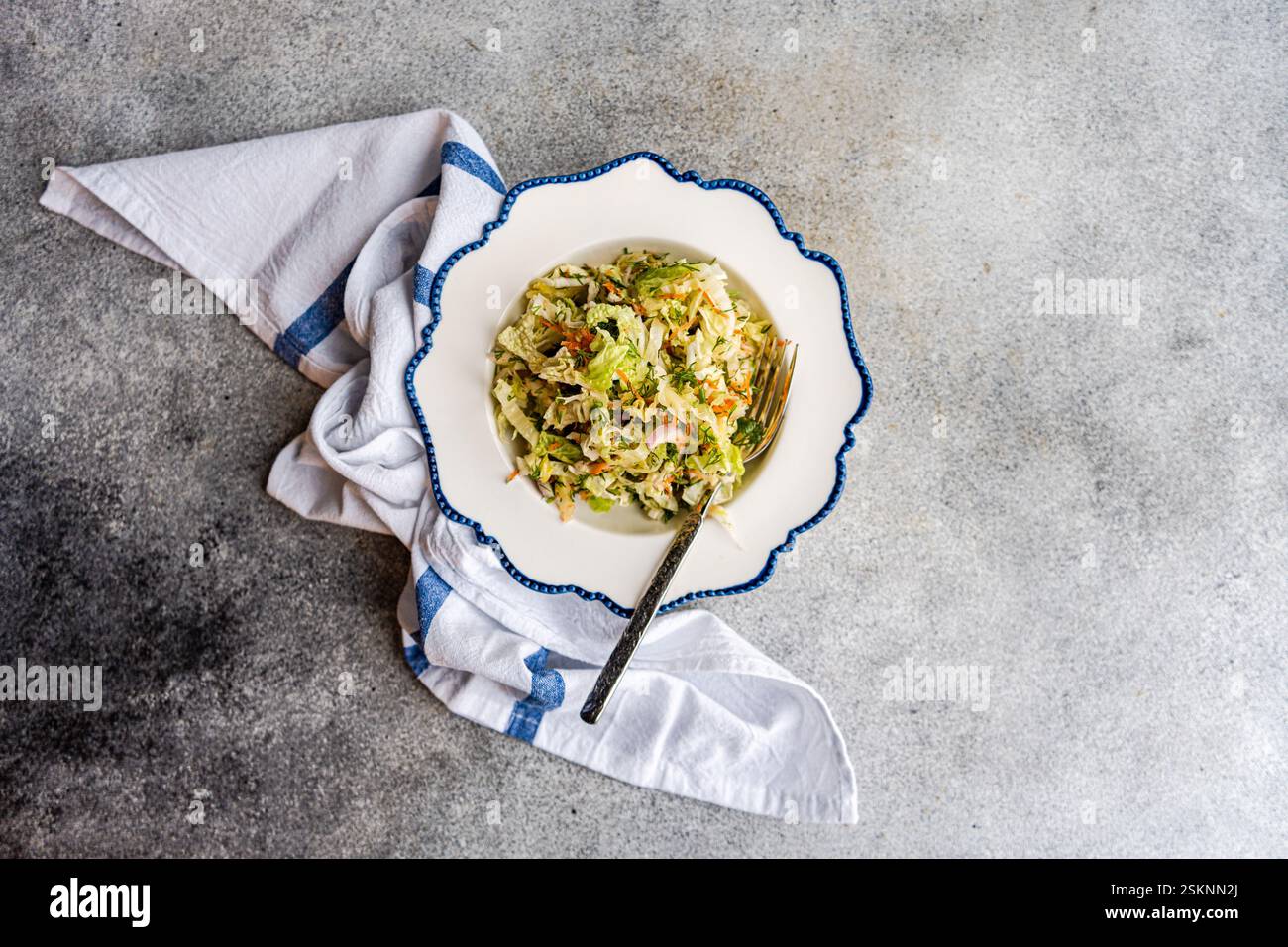 Vue aérienne d'un bol de salade de chou, carottes et oignons sur une table avec un torchon Banque D'Images