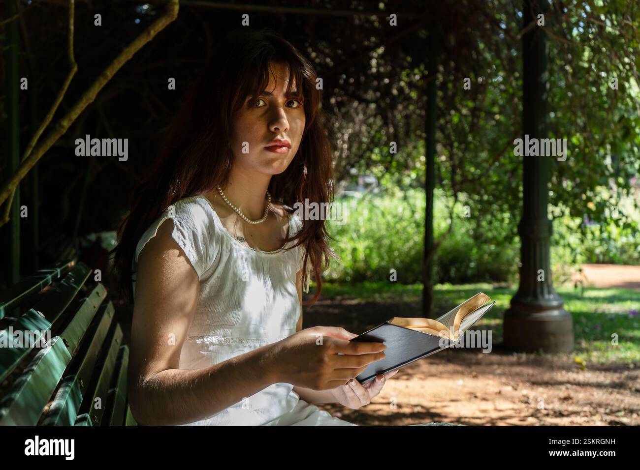 Étudiant serein appréciant la littérature dans un cadre paisible de parc, trouvant le réconfort et la connaissance au milieu de la beauté de la nature Banque D'Images