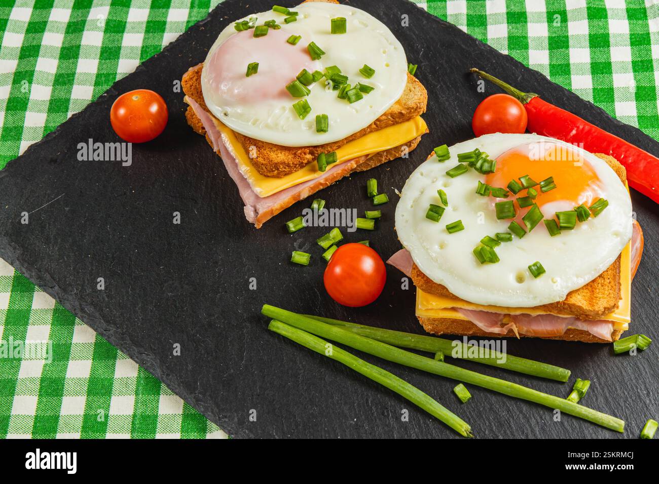 Deux sandwichs copieux pour le petit-déjeuner, garnis d'œufs ensoleillés et garnis d'oignons verts, servis avec des tomates cerises et un piment Banque D'Images