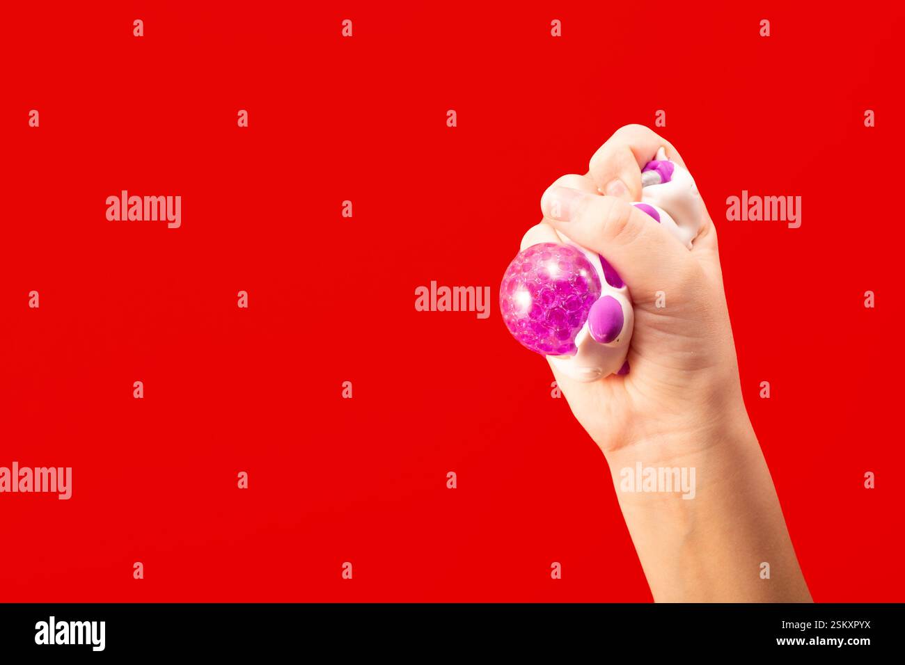 La main de l'enfant presse la boule de stress rose sur fond rouge. Concept de pensée positive. Copier l'espace Banque D'Images