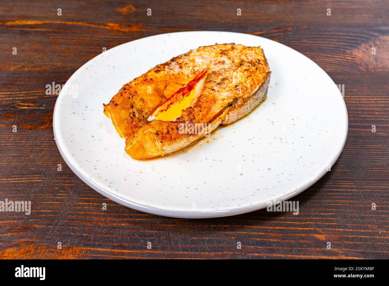 Un filet de saumon magnifiquement cuit se trouve sur une assiette blanche, mettant en valeur sa surface brun doré et légèrement garni, idéal pour un repas gastronomique Banque D'Images