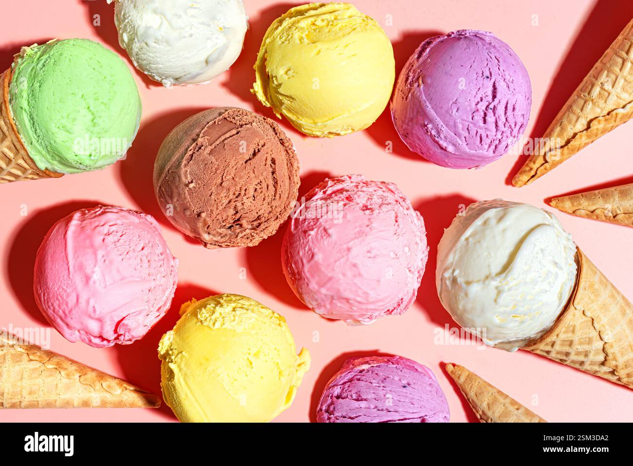 Cuillères à crème glacée assorties sur fond pastel rose, vue de dessus. Beaucoup de cuillères à crème glacée italienne bio et des cônes de gaufres, concept de dessert d'été. Banque D'Images