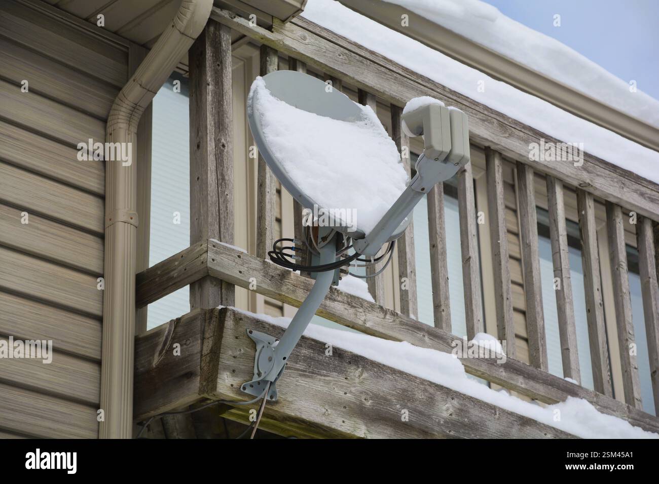 La neige s'accumule sur une antenne parabolique à la maison après une tempête de neige hivernale qui interrompt la télévision et le service Internet. Banque D'Images
