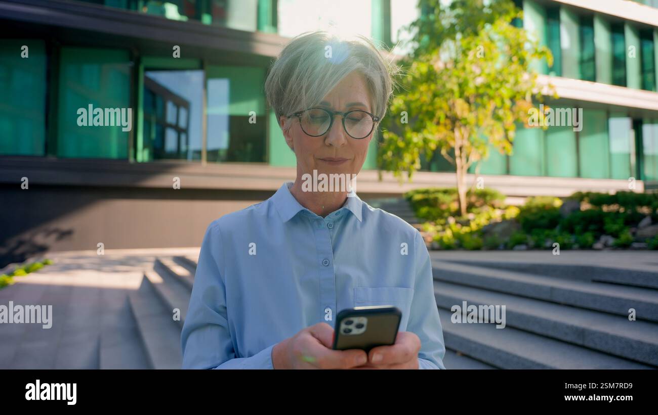 Réfléchie femme d'affaires mature aux cheveux gris des années 50 femme caucasienne senior femme tenir le téléphone pensant taper le message mobile chat messagerie entreprise mondiale Banque D'Images