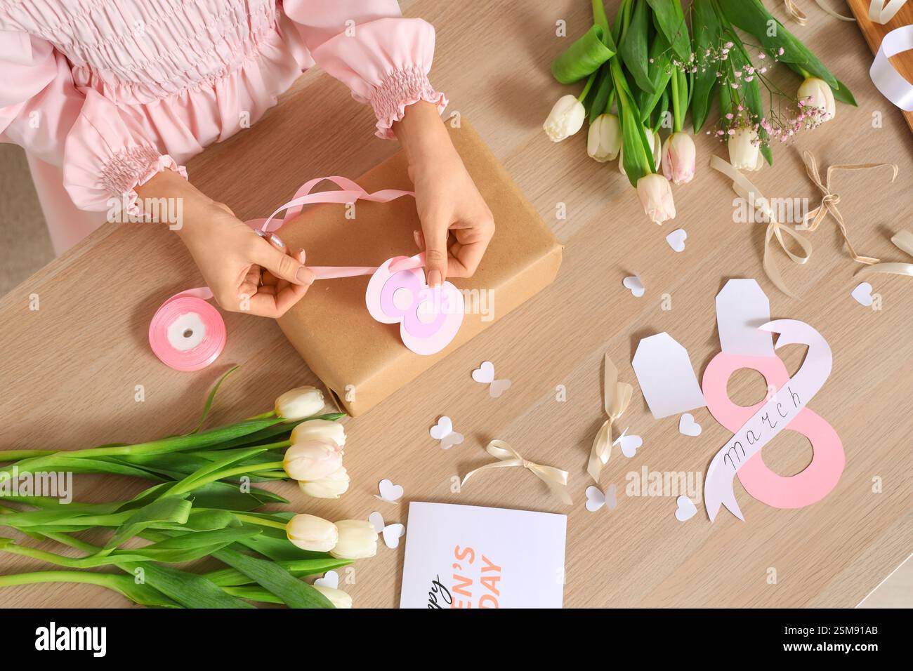 Femme avec boîte-cadeau, matériaux d'emballage et fleurs de tulipe pour la Journée internationale de la femme sur fond de bois Banque D'Images