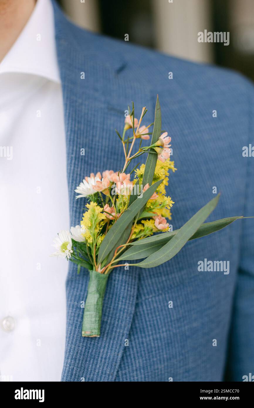 Une boutonnière élégante de fleurs roses et jaunes est épinglée à une veste de costume bleue, ajoutant une touche d'élégance. Banque D'Images