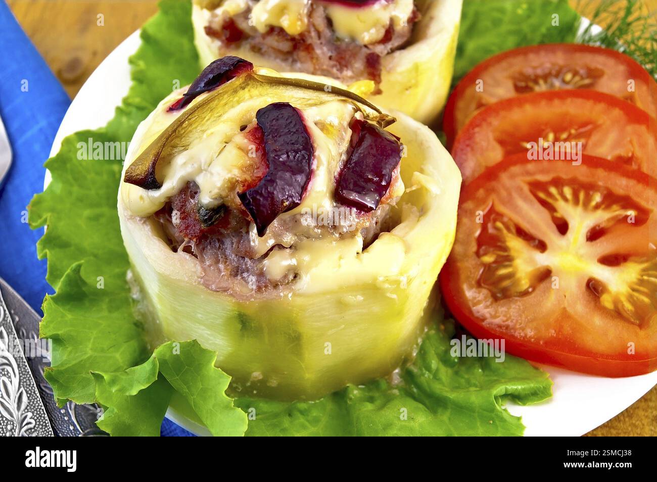 Courgettes farcies à la viande, mayonnaise, poivrons doux, tranchées â€‹ â€‹ prunes et tomates, laitue sur assiette blanche, serviette bleue, fourchette et couteau sur bois Banque D'Images