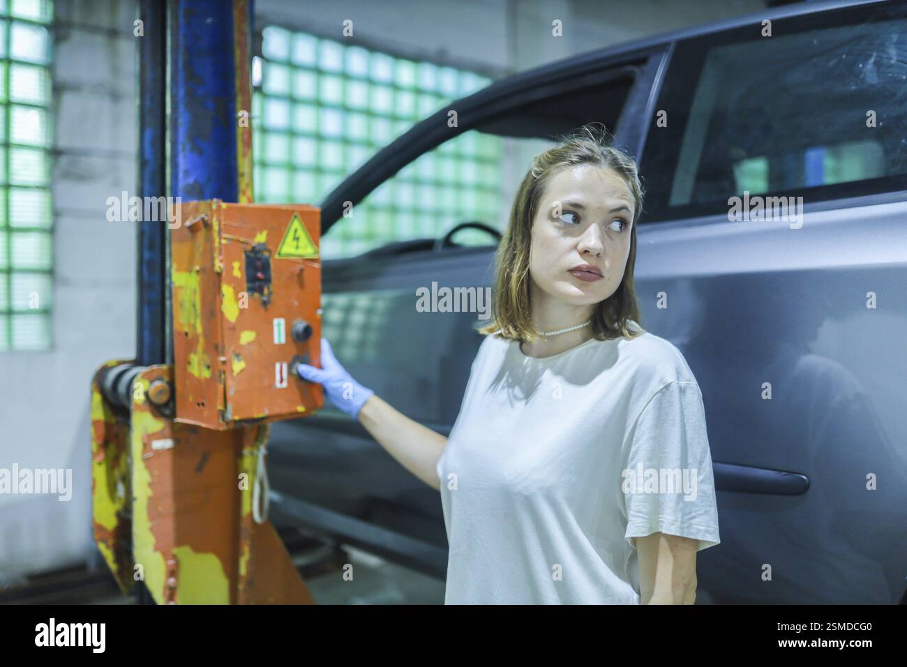 Une femme dans un atelier se tient près d'un ascenseur de voiture, regardant concentré sur la tâche, avec sa main sur un interrupteur Banque D'Images