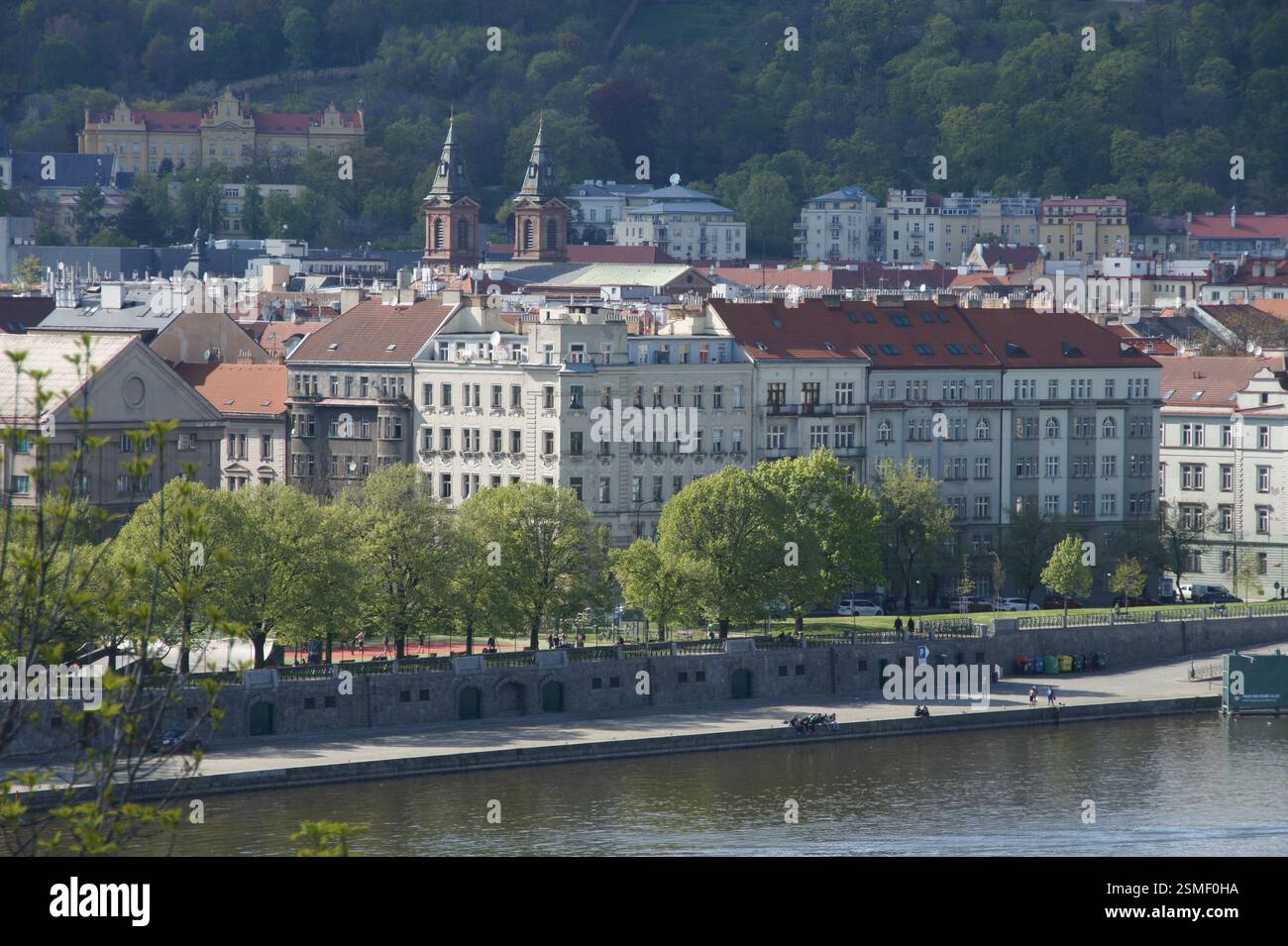 Paysage urbain. Des toits rouges bordent une rive, avec des arbres feuillus encadrant des bâtiments historiques et des églises. Une scène vibrante de la vie quotidienne dans une tête européenne Banque D'Images