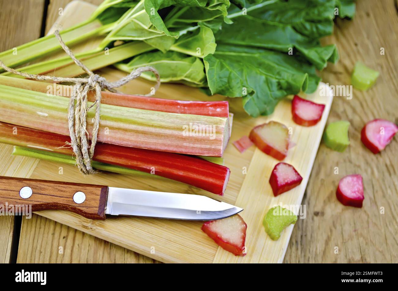 Ensemble de branches de rhubarbe, les morceaux de rhubarbe avec une feuille et un couteau sur une planche en bois Banque D'Images