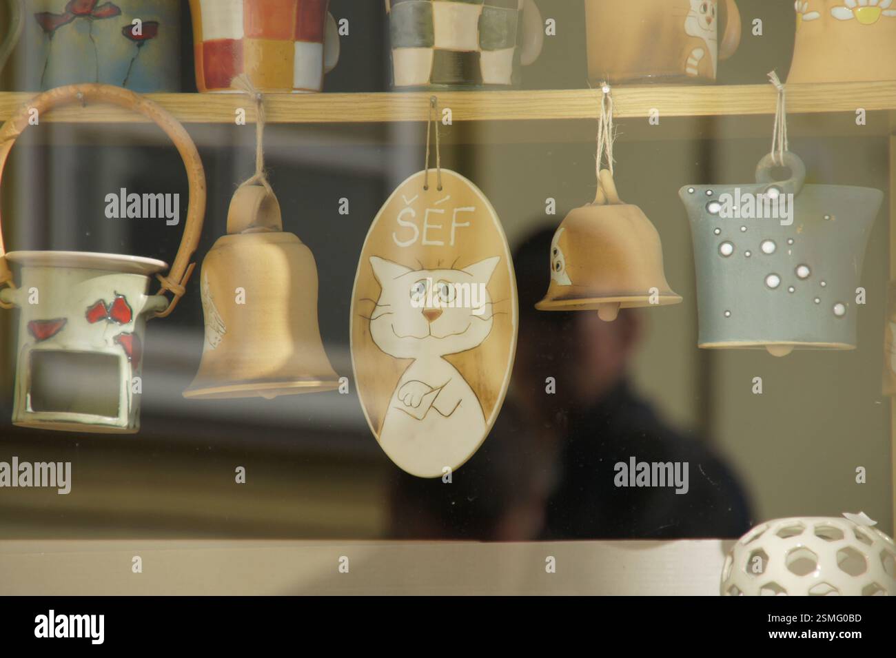 Figurine de chat en céramique suspendue sur une étagère avec des cloches et de la poterie. Chat heureux avec les bras croisés, disant 'Salut!'. 'Šéf' est tchèque pour 'Boss', indiquant un pla Banque D'Images