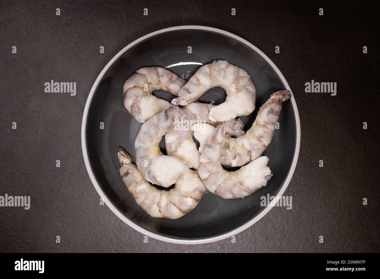 Crevettes tigrées crues congelées crevettes dans un bol gris sur une table de cuisine grise Banque D'Images