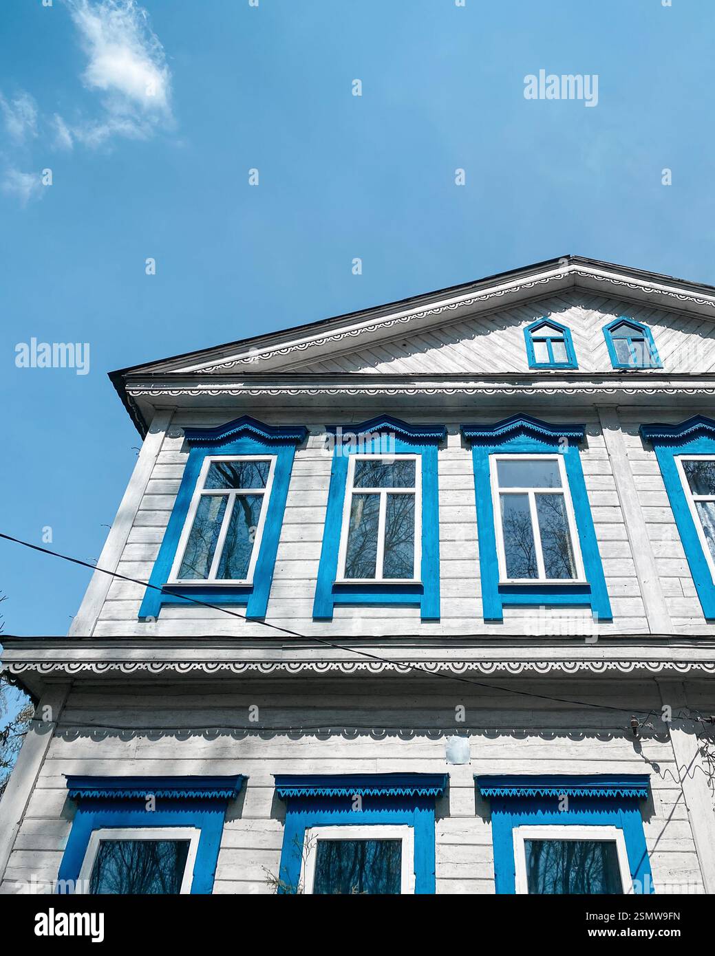 Vieille maison de deux étages avec façade peinte en blanc et fenêtre bleue entoure le ciel bleu clair. Banque D'Images