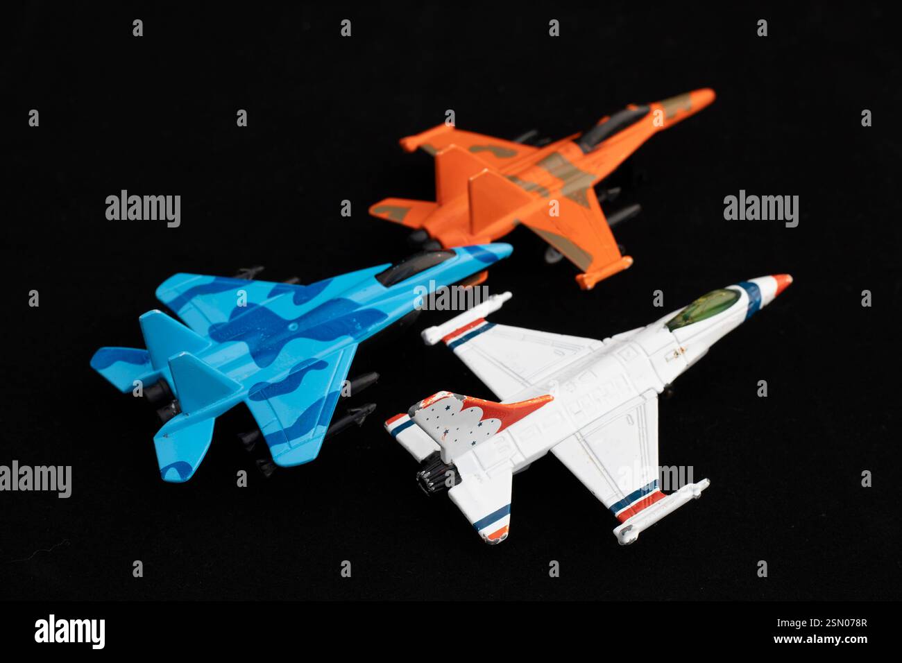 Ensemble de trois jets de chasse jouet en bleu, orange et blanc sur fond noir. Concept de modèles d'avions militaires. Banque D'Images