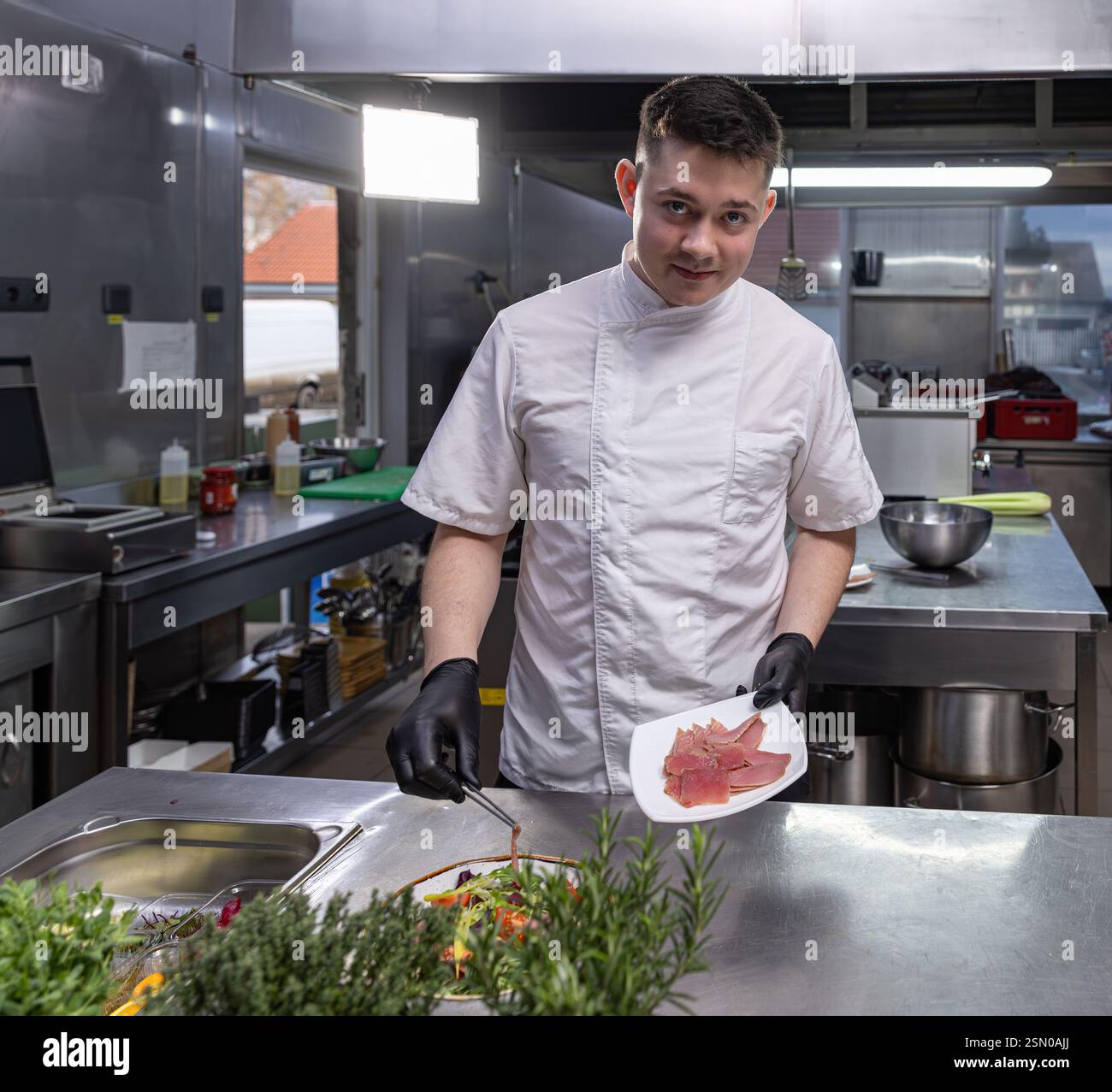 Jeune chef ajoutant du saumon fumé à une salade fraîche dans la cuisine du restaurant Banque D'Images