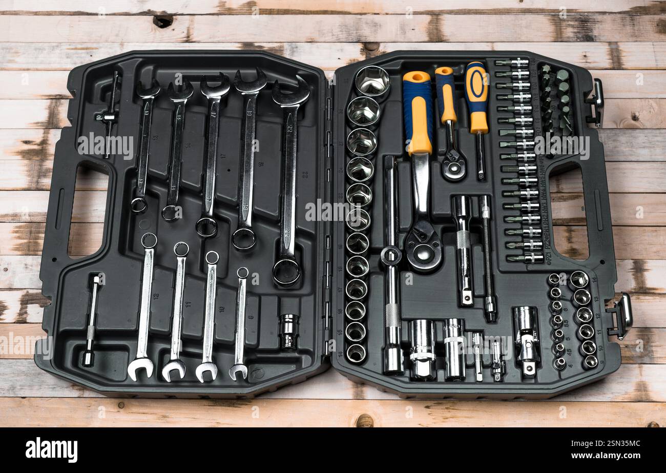 Trousse à outils complète avec diverses clés et douilles organisées dans un boîtier noir sur une surface en bois Banque D'Images
