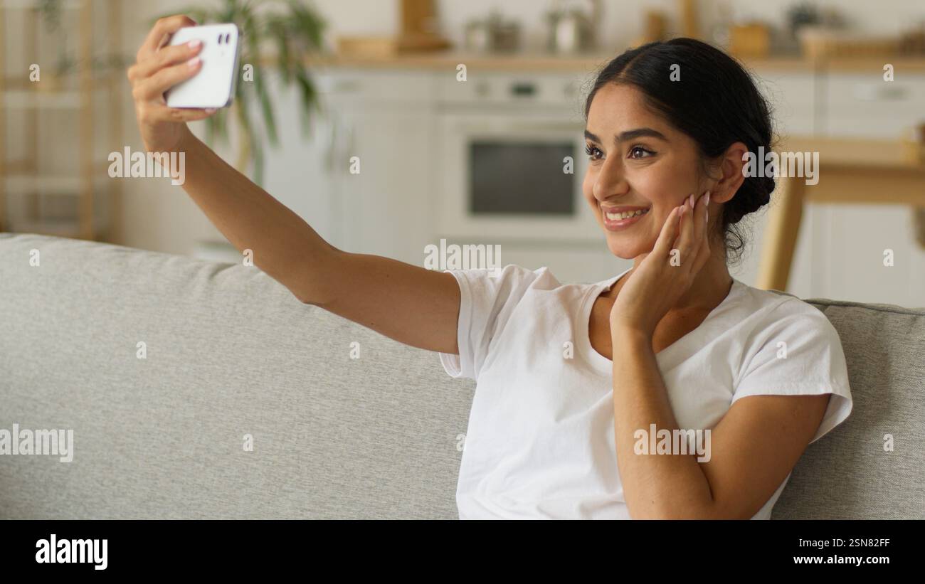 Indienne femme souriante influenceur vlogger blogueur Arabian Girl femme faire selfie photo avec téléphone portable posant canapé assis canapé à la maison smartphone Banque D'Images