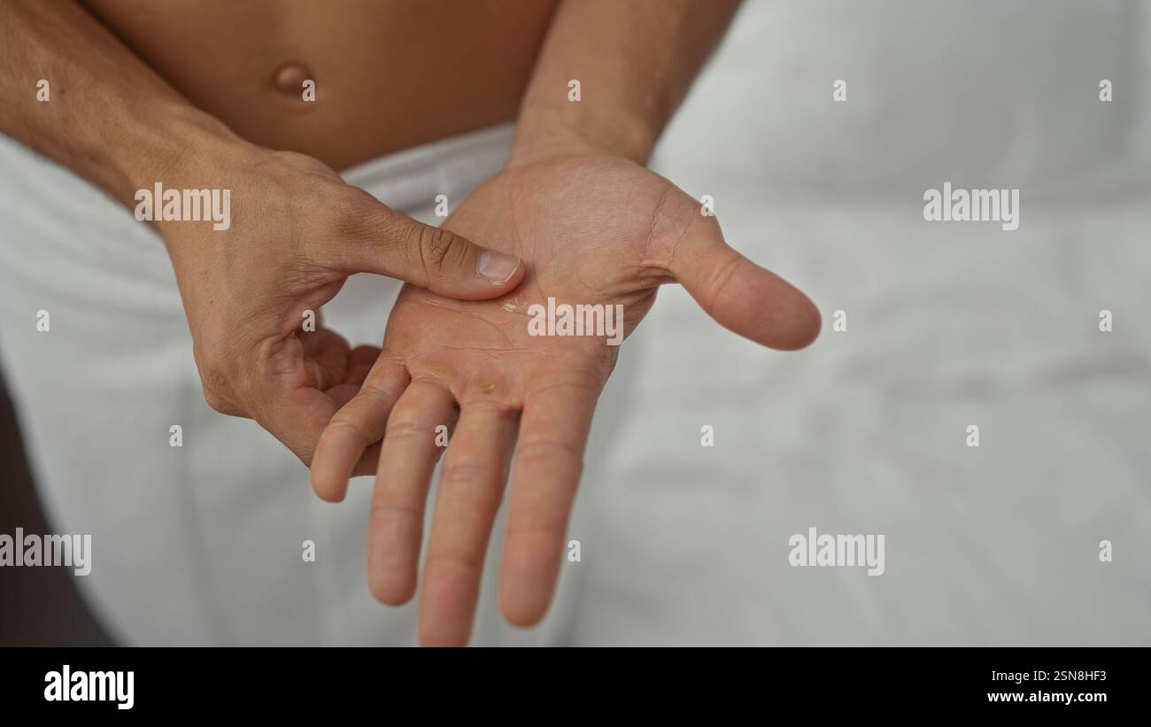 Jeune homme hispanique examinant les mains à l'intérieur, montrant des lignes et des textures détaillées de la paume dans un cadre domestique, illustrant les soins personnels et l'introspection. Banque D'Images