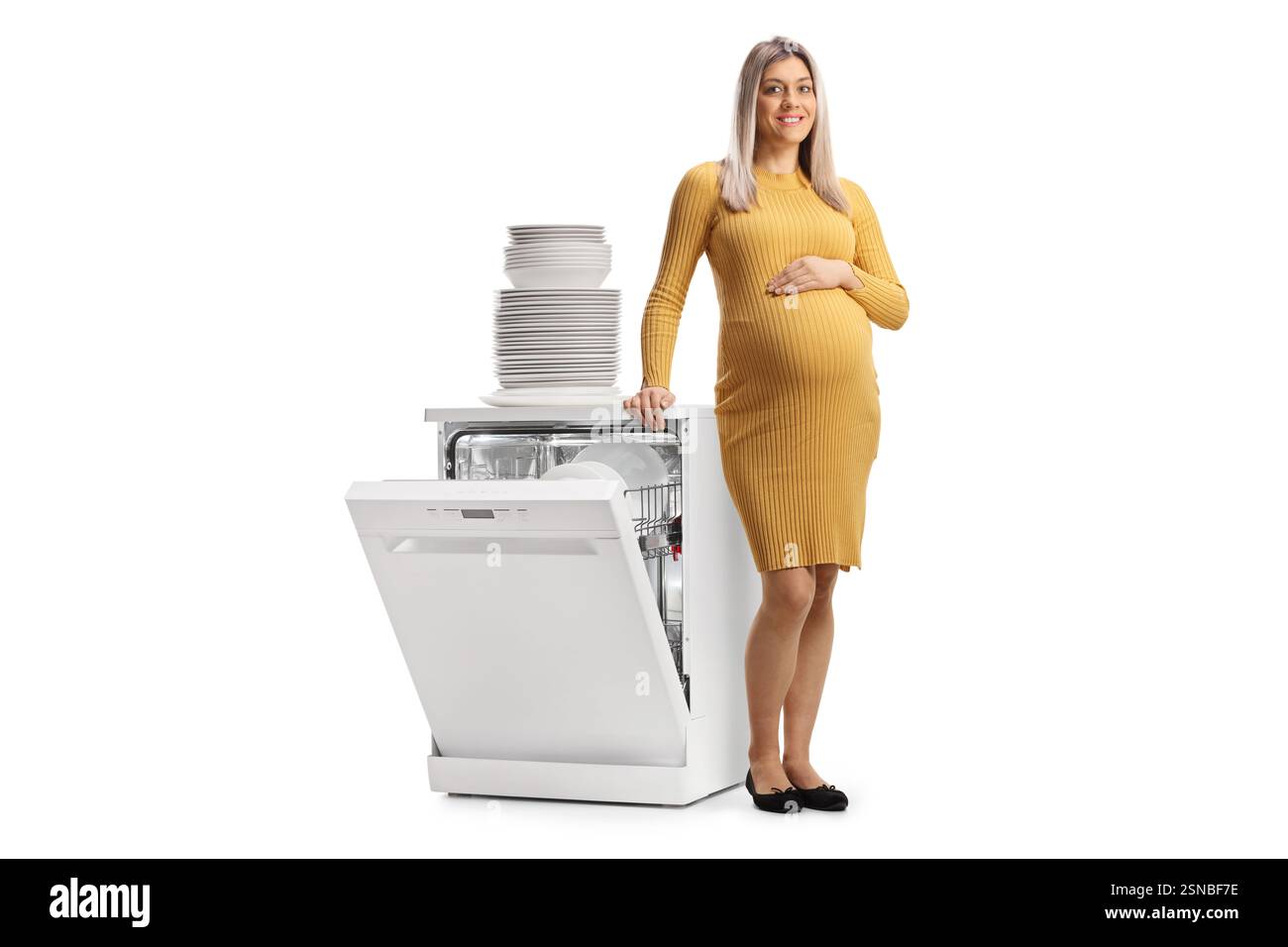 Femme enceinte appuyée sur un lave-vaisselle avec une pile de vaisselle propre isolée sur fond blanc Banque D'Images