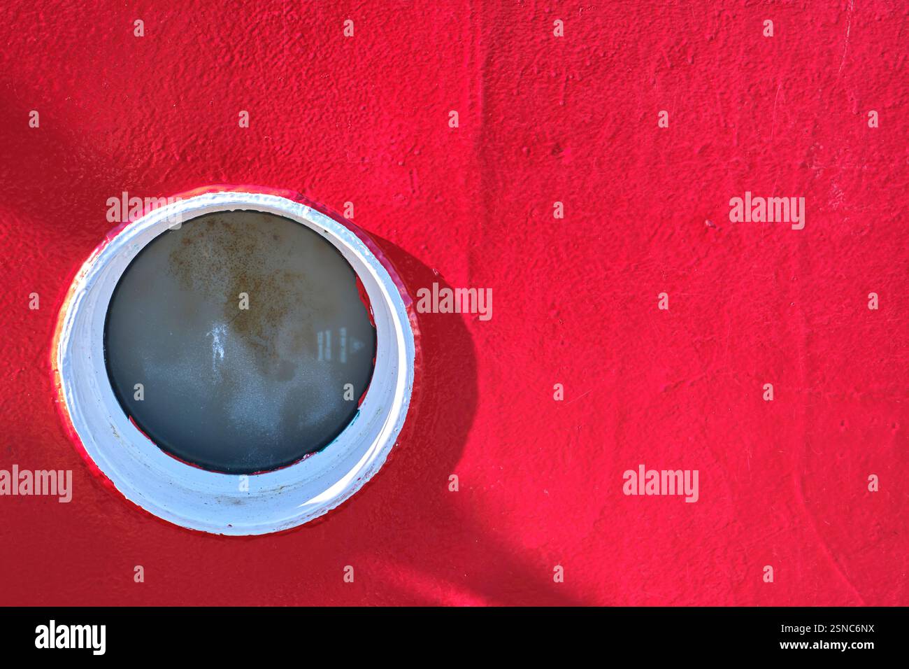 La fenêtre circulaire contraste avec une texture rouge éclatante sur une coque de navire. Colindres, cantabrie, espagne Banque D'Images