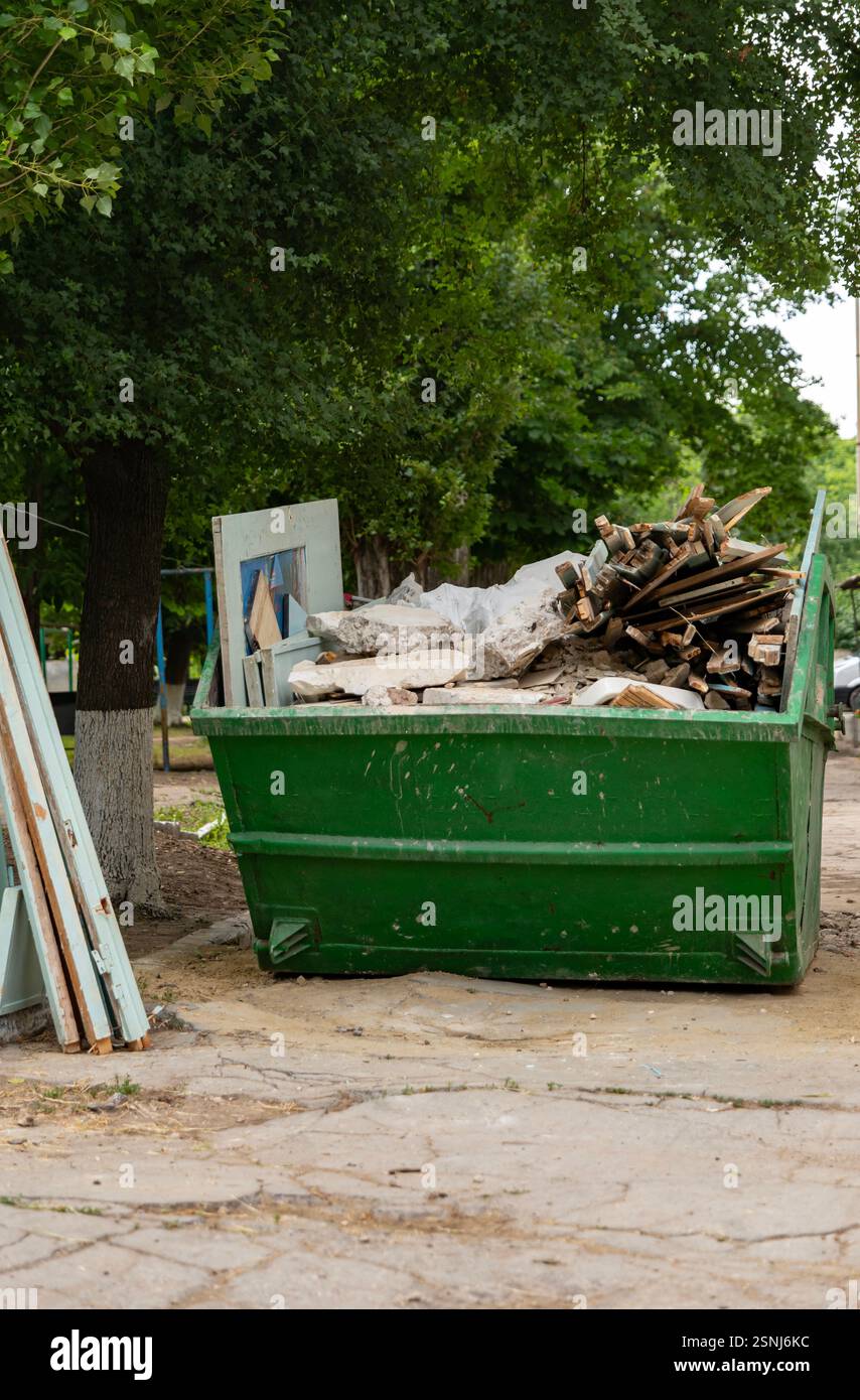 Conteneur de déchets industriels rempli de déchets de construction, situé dans la cour du bloc. Photo verticale. Banque D'Images