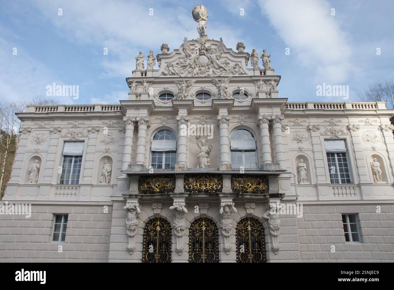 Un grand palais blanc à Munich, en Allemagne, avec un balcon orné d'une statue. Les détails architecturaux complexes et la nature environnante créent un pictu Banque D'Images