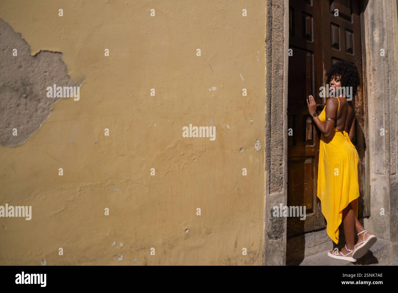 Portrait d'une belle femme portant une robe jaune debout par une vieille porte en bois brun. Concept de voyage de personne heureuse. Banque D'Images