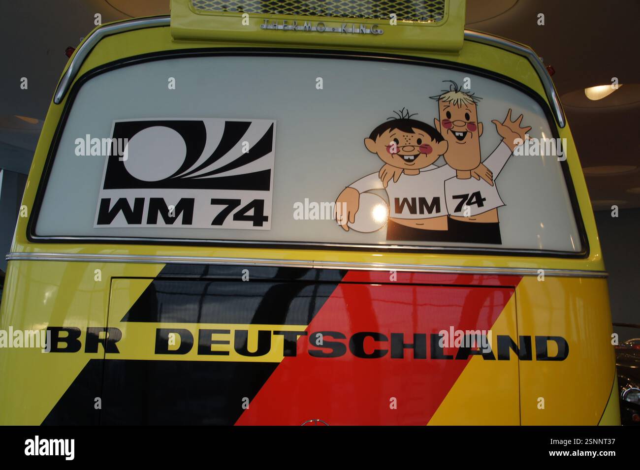 Un bus jaune avec 'WM 74' et des figures de dessins animés a 'BR DEUTSCHLAND' écrit en bas. C'est probablement un bus promotionnel pour le thé ouest-allemand Banque D'Images