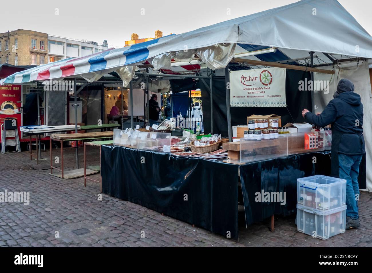 Stand de marché extérieur proposant des plats et des spécialités espagnoles artisanales, mettant en vedette les vendeurs locaux dans un cadre urbain animé à Cambridge Market. Banque D'Images