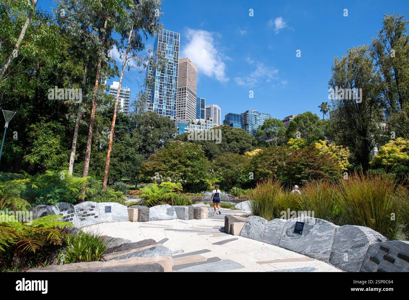 Une fille se promène dans le jardin commémoratif JFK avec ses fougères, ses herbes, ses arbres et ses arbustes dominés par les gratte-ciel de treasury Gardens Melbourne Banque D'Images
