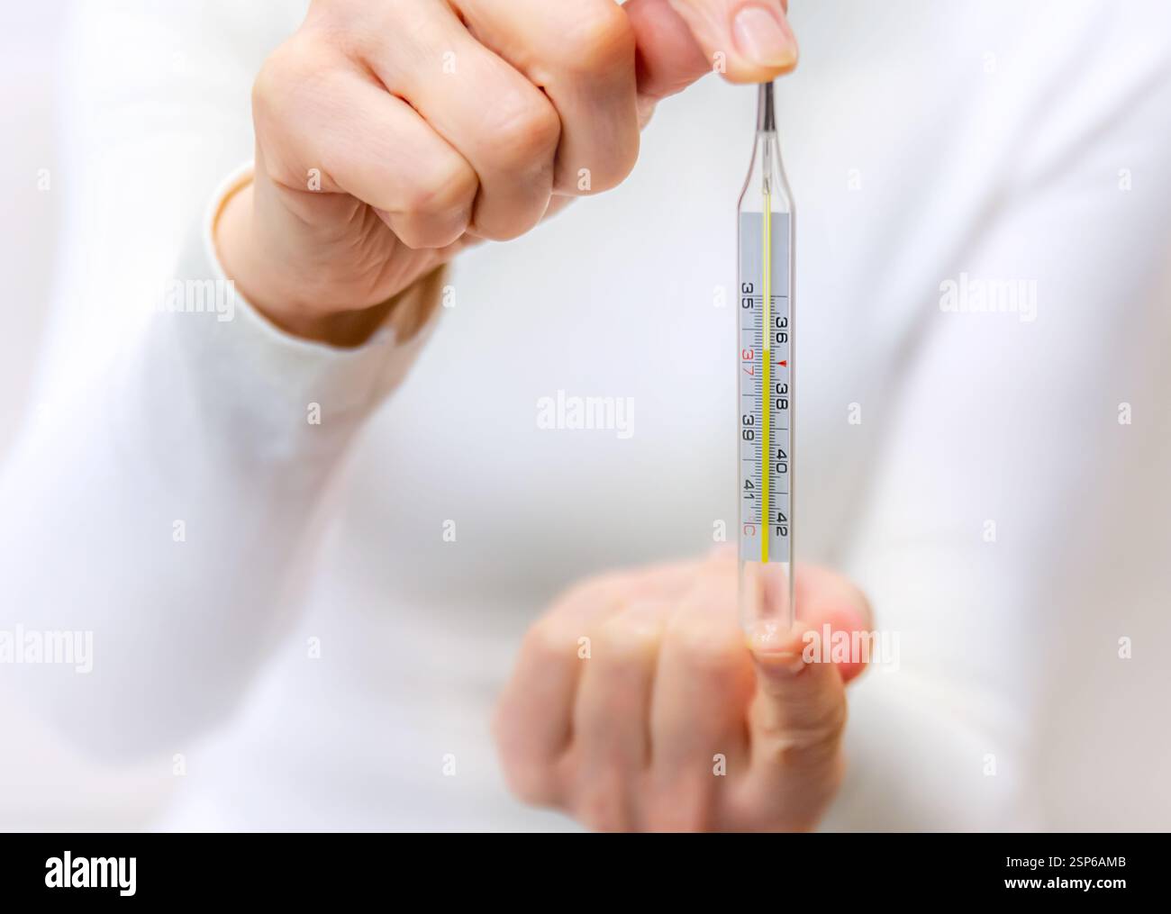 Une personne tient un thermomètre en verre indiquant la température corporelle avec une légère préoccupation dans un cadre intérieur bien éclairé Banque D'Images