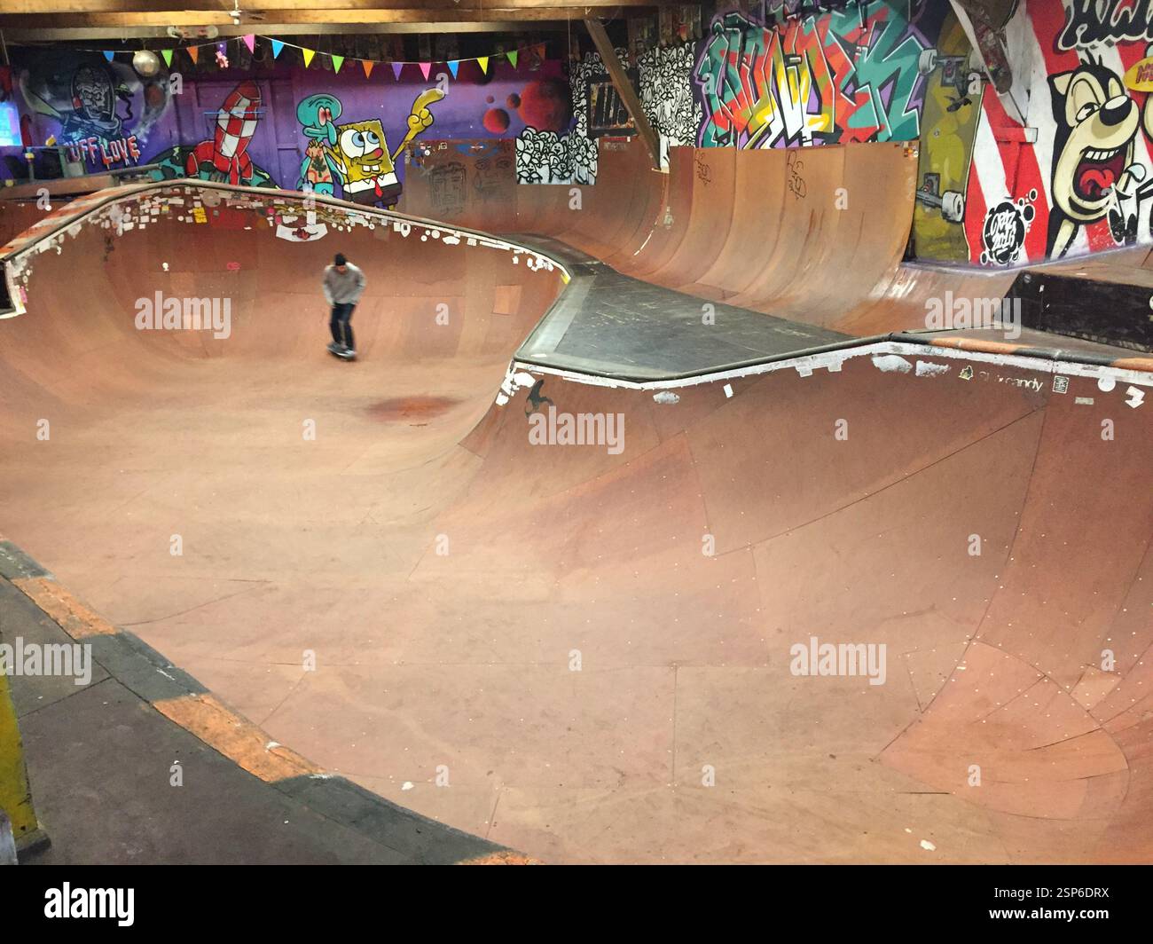 Un jeune patineur met en valeur ses compétences tout en manœuvrant à travers un parc de skatepark intérieur spacieux orné de graffitis colorés Banque D'Images
